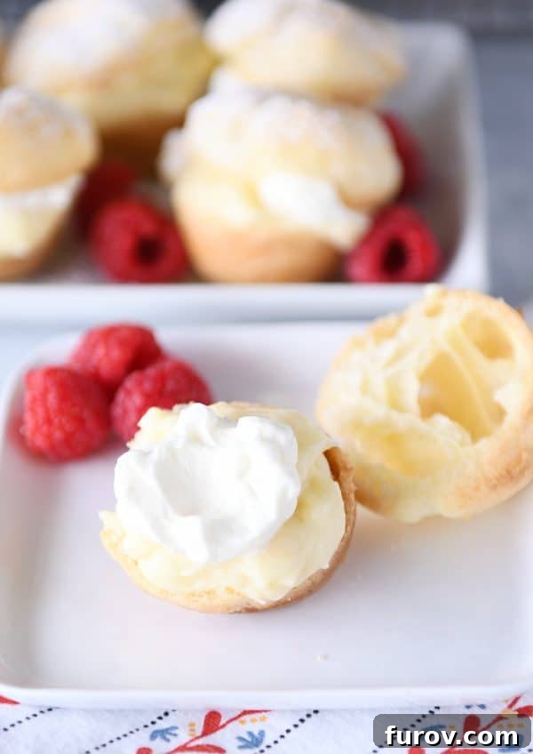 A pristine cream puff, artfully split open, revealing layers of rich cream filling and a scattering of fresh raspberries on a white plate, ready to be enjoyed.