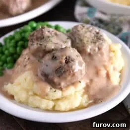 Three meatballs on top of pile of mashed potatoes smothered in thick brown gravy.