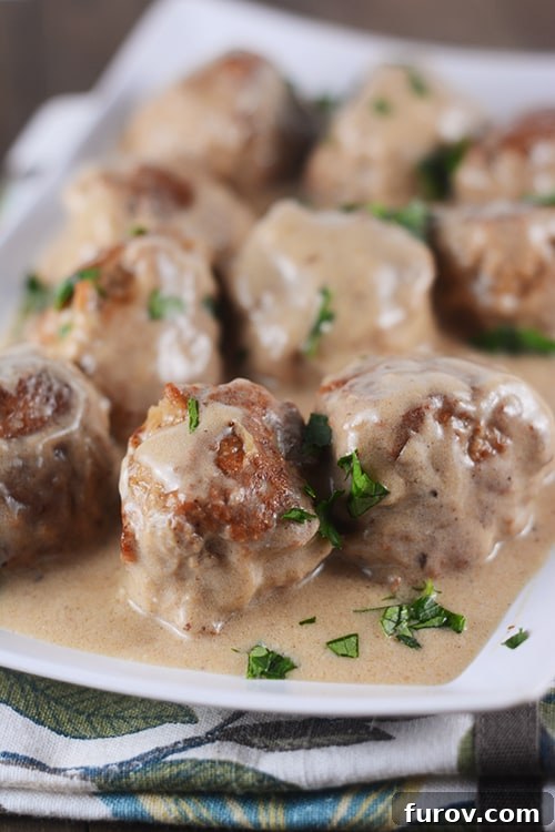 Creamy Skillet Swedish Meatballs 12 A beautiful white platter overflowing with perfectly golden brown cooked meatballs and a rich, velvety gravy, gently sprinkled with fresh green herbs.