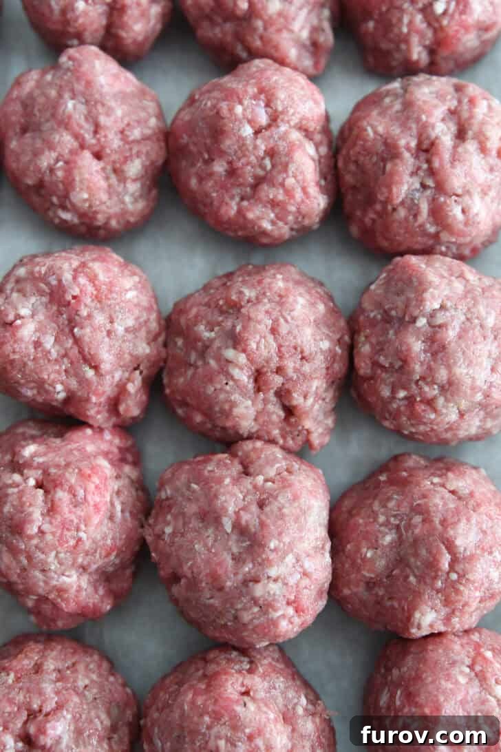 Creamy Skillet Swedish Meatballs 4 Top-down view of nine perfectly formed, unbaked meatballs arranged neatly on a sheet of parchment paper, awaiting their skillet journey.