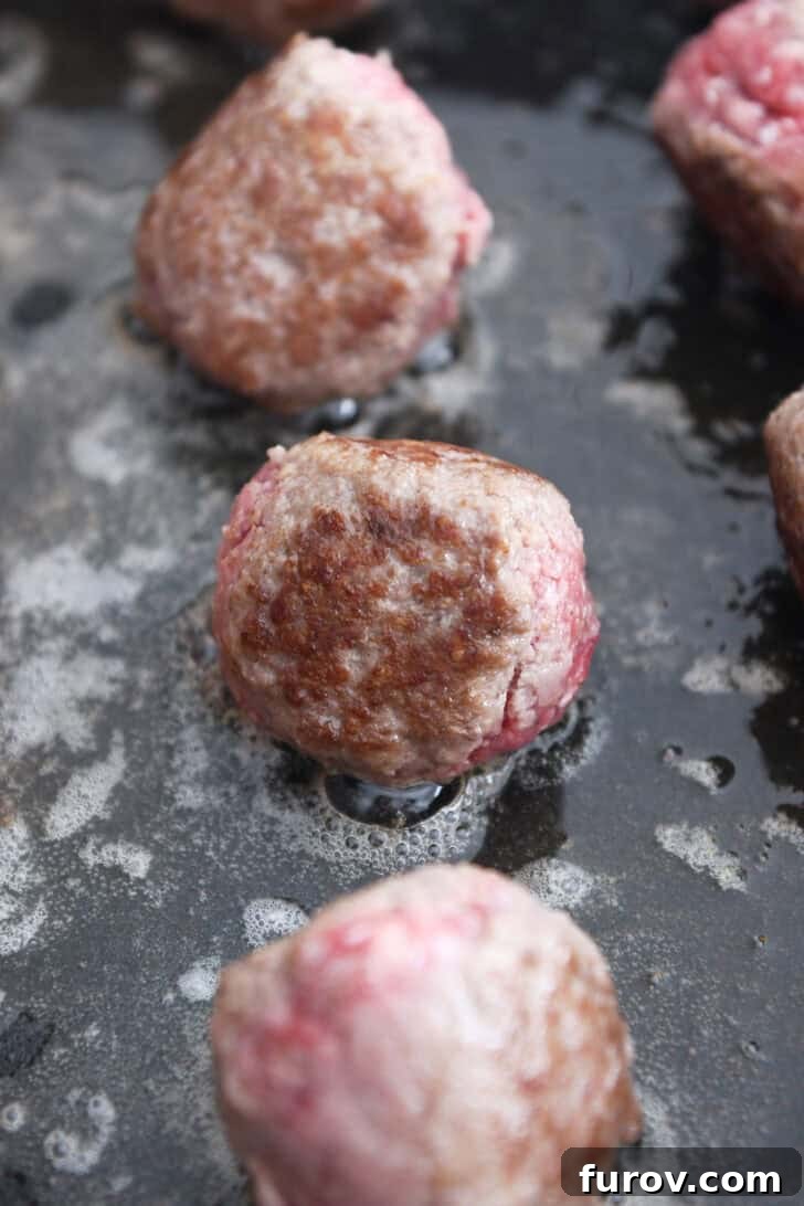 Creamy Skillet Swedish Meatballs 5 Close-up shot of partly browned meatballs sizzling in an electric skillet, bathed in a mixture of butter and olive oil, developing a delicious crust.