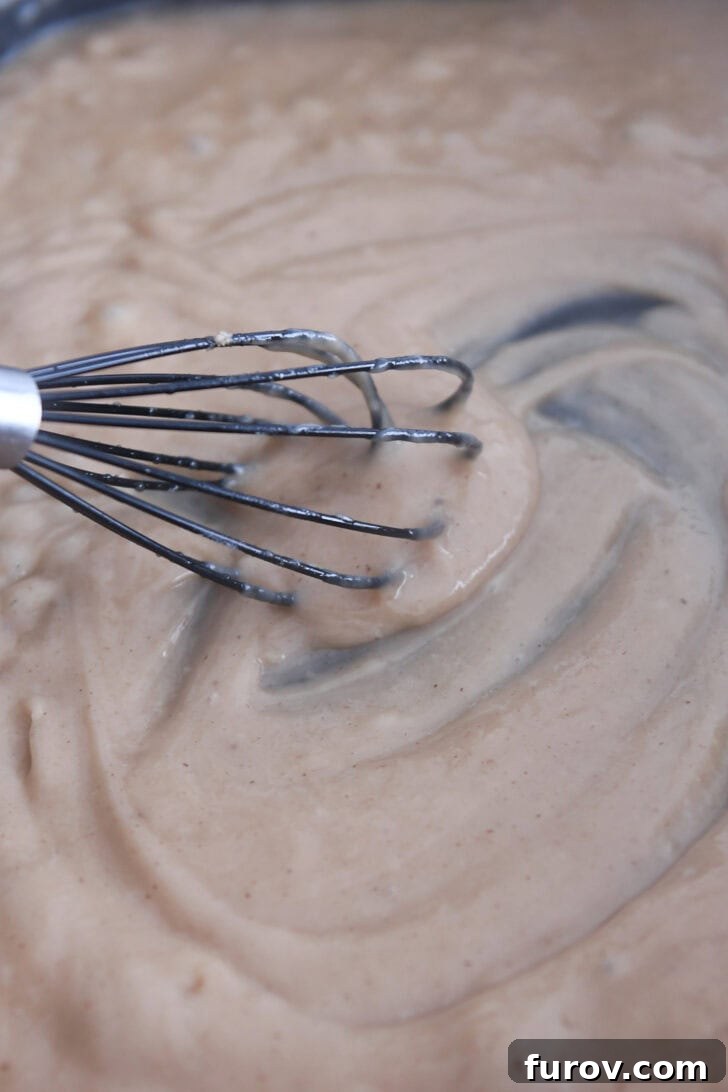 Creamy Skillet Swedish Meatballs 6 Electric skillet filled with a thick, glossy brown gravy, expertly whisked to a smooth consistency, forming the delicious base for Swedish meatballs.