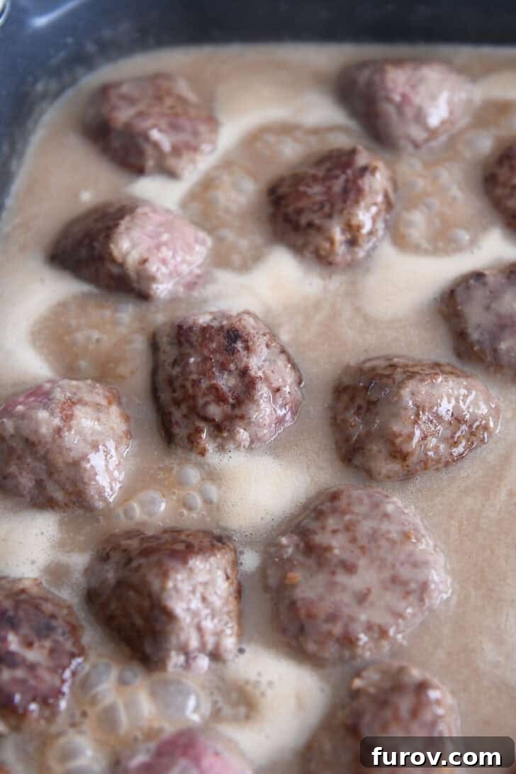 Creamy Skillet Swedish Meatballs 7 Golden brown meatballs simmering gently in a rich, velvety brown gravy sauce within an electric skillet, absorbing all the wonderful flavors.