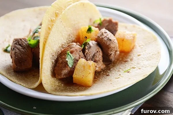 Close-up view of two sweet and spicy pork and pineapple tacos in corn tortillas, showcasing the vibrant filling.
