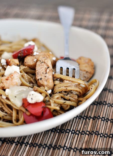 Close-up of a white bowl featuring perfectly cooked linguine, succulent chicken, and vivid red pepper pieces, highlighting the dish's rich textures and appealing colors.