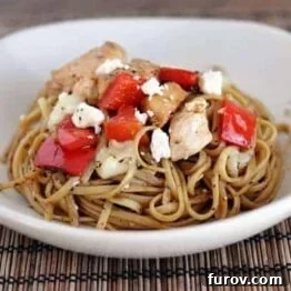 A vibrant Balsamic Chicken Noodle Bowl with golden linguine, tender chicken pieces, bright red peppers, and a sprinkle of cheese.
