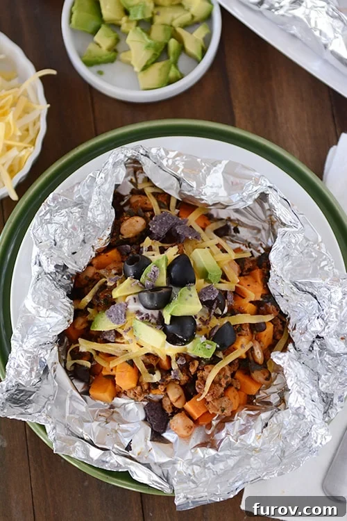 Foil Roasted Sweet Potato Tacos 2 Top view of a tinfoil packet of a cooked sweet potato taco mixture topped with cheese, avocado and sliced olives.