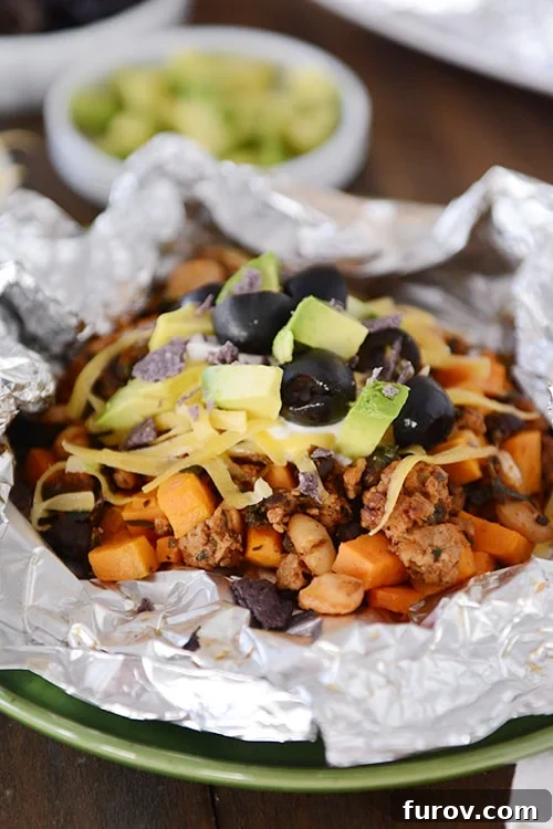 Foil Roasted Sweet Potato Tacos 4 An open tinfoil packet of cooked sweet potato tacos toped with cheese, sour cream, avocado dices, and slices olives.