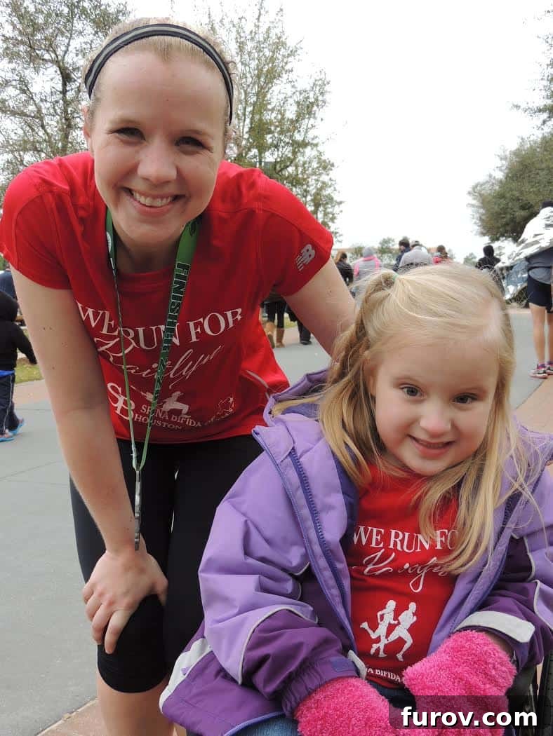 A mother gently pushing her young daughter in a wheelchair, both smiling.