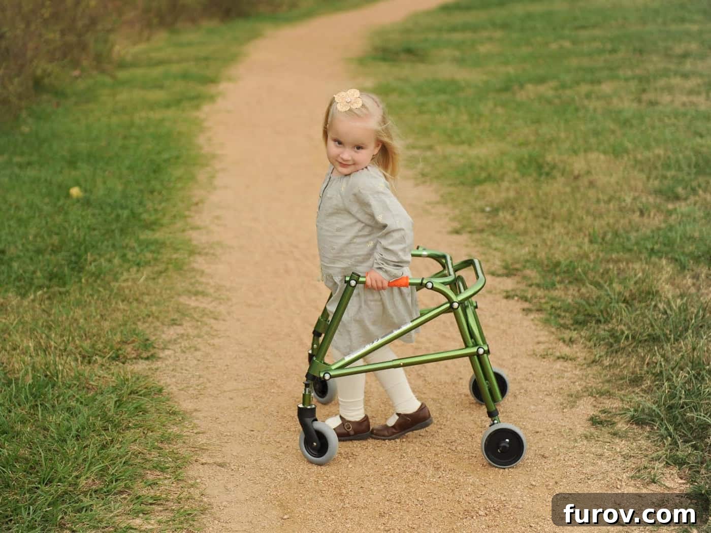 A determined little girl using a walker on a dirt path, celebrating her independence.