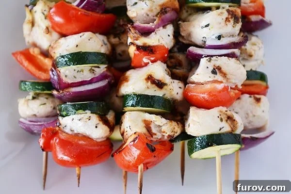 Zesty Greek Chicken Skewers with Cool Tzatziki 3 Top view of several grilled Greek chicken and vegetable kebabs stacked on a serving dish, ready to be enjoyed.
