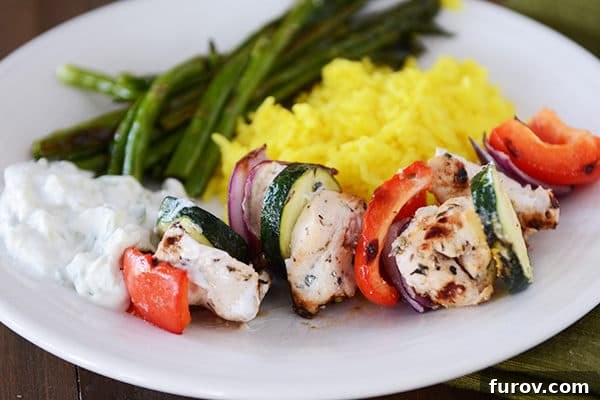 Zesty Greek Chicken Skewers with Cool Tzatziki 4 A close-up of grilled chicken and vegetable kebabs served alongside fresh green beans and a bowl of creamy tzatziki sauce.