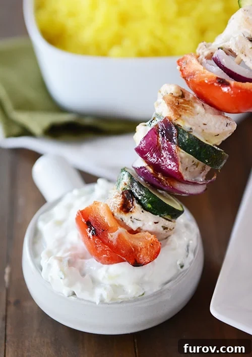 Zesty Greek Chicken Skewers with Cool Tzatziki 5 A grilled Greek chicken kebab being generously dipped into a bowl of homemade tzatziki sauce.
