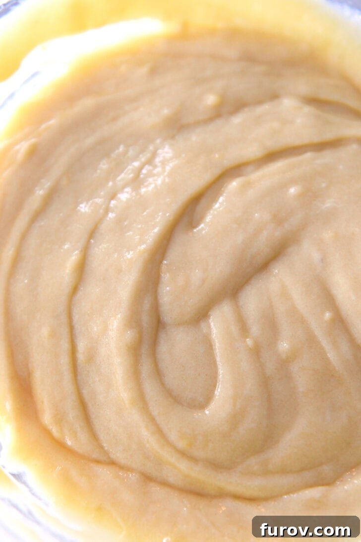Top down view of a glass bowl containing a vibrant, smooth lemon batter, perfectly mixed and ready for baking.