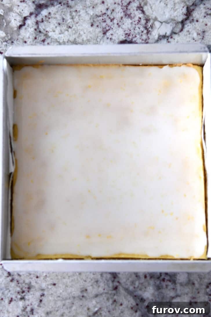 Top down view of a metal pan filled with cooked and evenly glazed lemon brownie batter, glistening and ready for chilling.