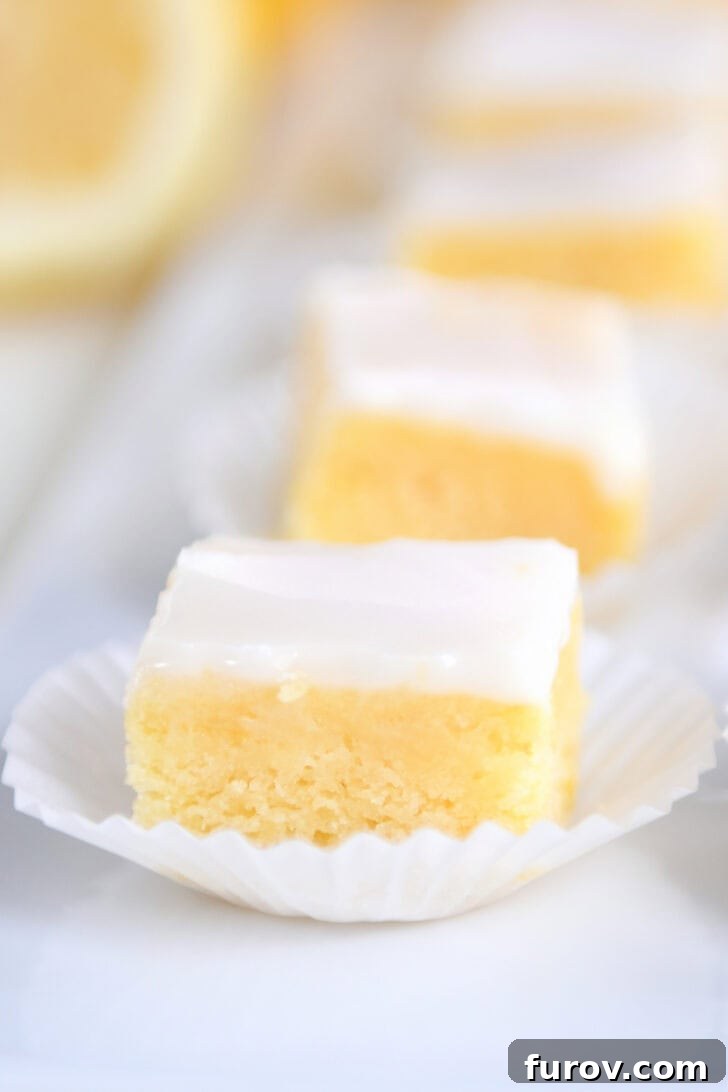 A beautiful line of lemon brownie squares, each topped with a luscious white glaze and neatly placed in white muffin cups on a pristine white serving platter, ready to be enjoyed at any gathering.
