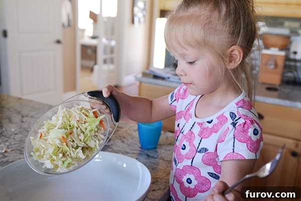 A little girl pouring shredded cabbage into a large white platter.