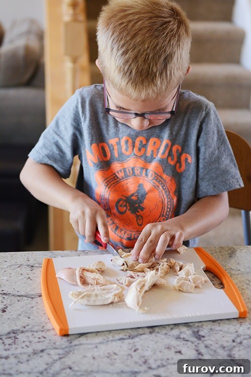 A little boy cutting up chicken on a cutting board.