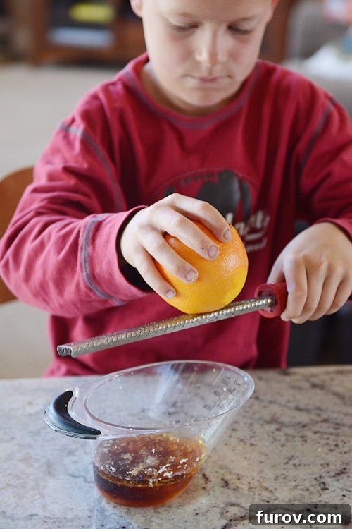 A little boy grating an orange over a microplane.