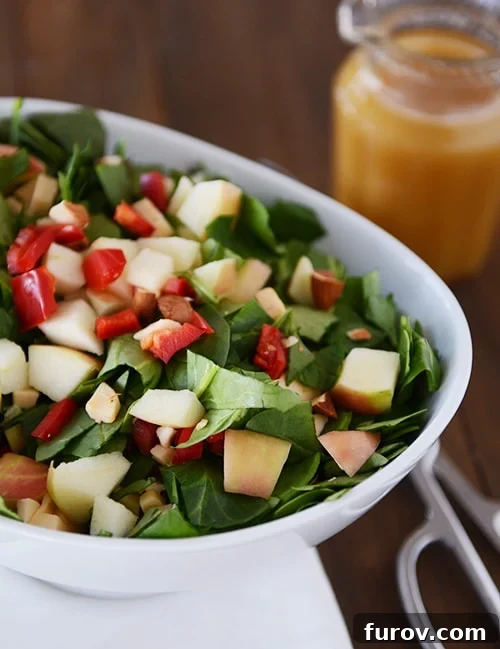 A white bowl full of chopped spinach salad with gouda, apples, and peppers. 