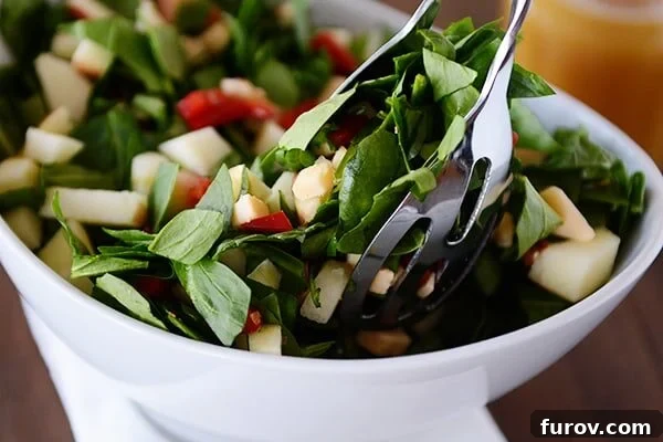 White bowl of chopped spinach and gouda salad with tongs taking a scoop out.