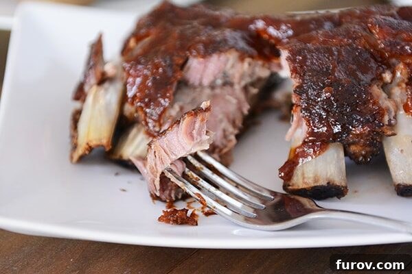 Slow Cooker Fall-Off-The-Bone Root Beer BBQ Ribs 3 A fork piercing into a section of tender baby back ribs, showcasing the succulent meat effortlessly separating from the bone, highlighting the recipe's fall-off-the-bone promise.