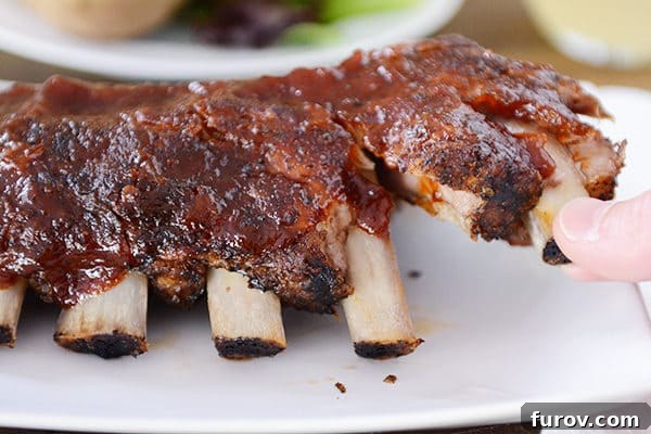 Slow Cooker Fall-Off-The-Bone Root Beer BBQ Ribs 4 Two perfectly cooked ribs being gently pulled away from the main rack, demonstrating the exceptional tenderness and 'fall-off-the-bone' quality achieved with this slow cooker method.