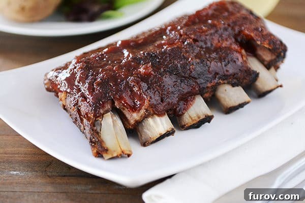 Slow Cooker Fall-Off-The-Bone Root Beer BBQ Ribs 5 A pristine white platter proudly displays a full rack of perfectly cooked baby back ribs, generously coated in a rich, dark BBQ sauce, ready to be served and savored.