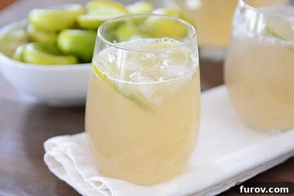 Two glasses of iced ginger mint limeade in front of a bowl of sliced limes, garnished with fresh mint.