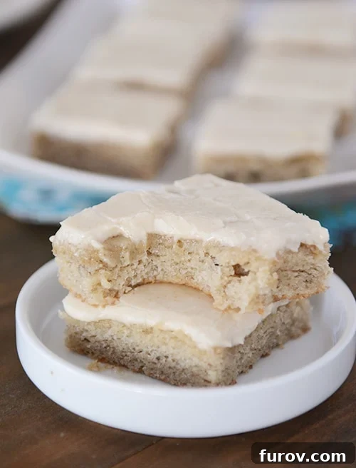 Two soft and moist banana bars, stacked on a plate, with a corner bite taken out of the top bar, revealing its delightful texture and the browned butter frosting.