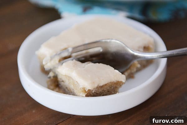 An iced banana bar with a fork taking a bite out, showcasing the creamy browned butter frosting and the tender cake beneath.