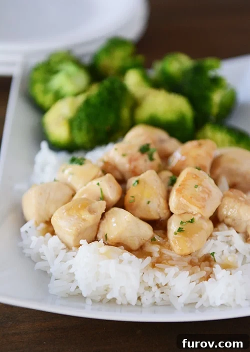 A white platter of cooked rice topped with lemon-glaze chicken next to a helping of broccoli.