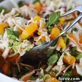 Mandarin Orange Chicken Salad in a white bowl, glistening with dressing, ready to be served.