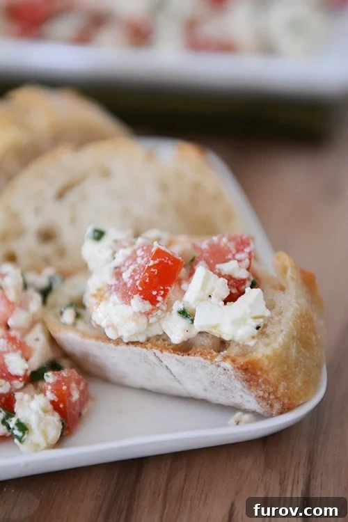 A sliced baguette topped with a generous portion of a vibrant Greek feta dip, showcasing its fresh ingredients.