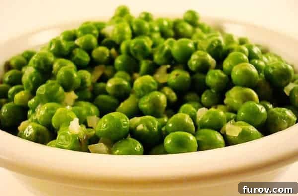 A crisp white bowl generously filled with tender, perfectly cooked buttery peas, ready to be served as a delightful side dish.