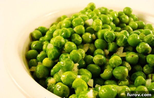 Close-up shot of vibrant green peas simmering in a skillet with sautéed garlic and onion, highlighted by golden butter and fresh thyme sprigs.