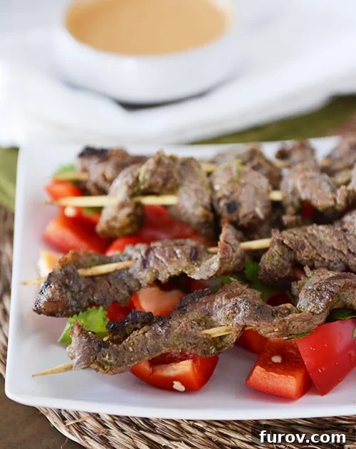 Quick and Easy Thai Beef Satay 2 A white tray of grilled beef skewers on top of chunks of raw red peppers, ready to be served.