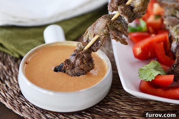 Quick and Easy Thai Beef Satay 3 A grilled beef skewer being dipped into a small ramekin of creamy Thai peanut sauce, highlighting the rich flavors.