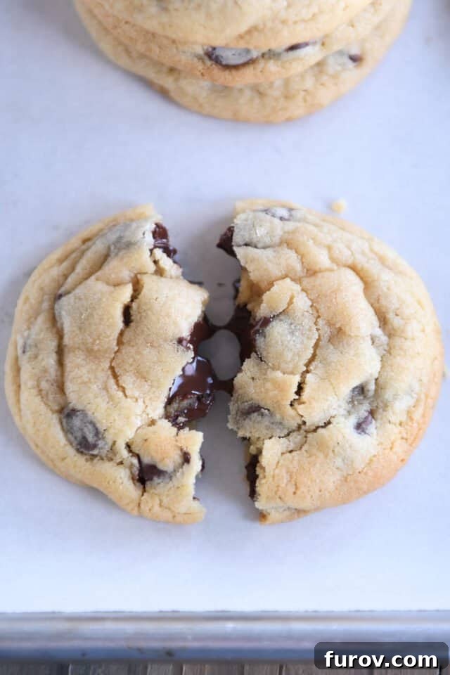 Super soft chocolate chip cookie broken in half on sheet pan.