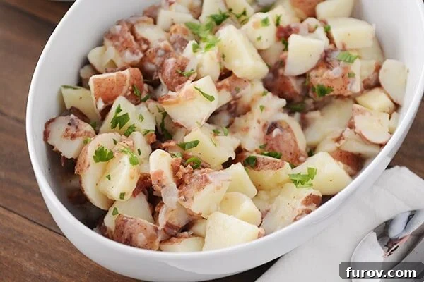 An oval bowl full of German potato salad topped with chopped parsley, showcasing the appetizing final presentation.