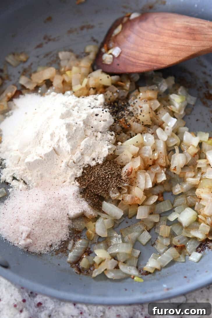 Top down view of a skillet with spices, sautéed onions, and flour, illustrating the dressing preparation.