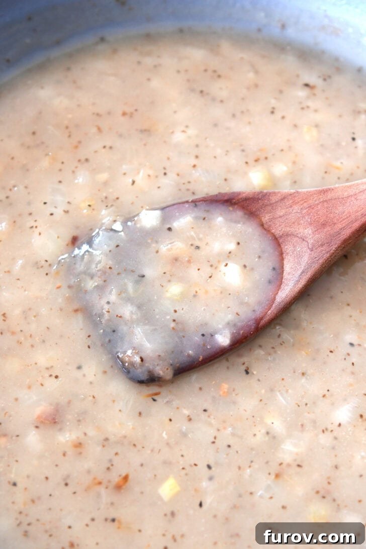 A wooden spoon stirring a skillet full of a creamy, white onion sauce, indicating the thickened dressing.