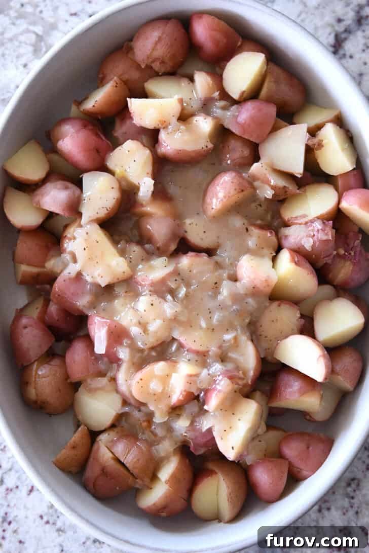 Top down view of a white oval dish with large potato chunks and an onion sauce spread over the top, illustrating the dressing being added.