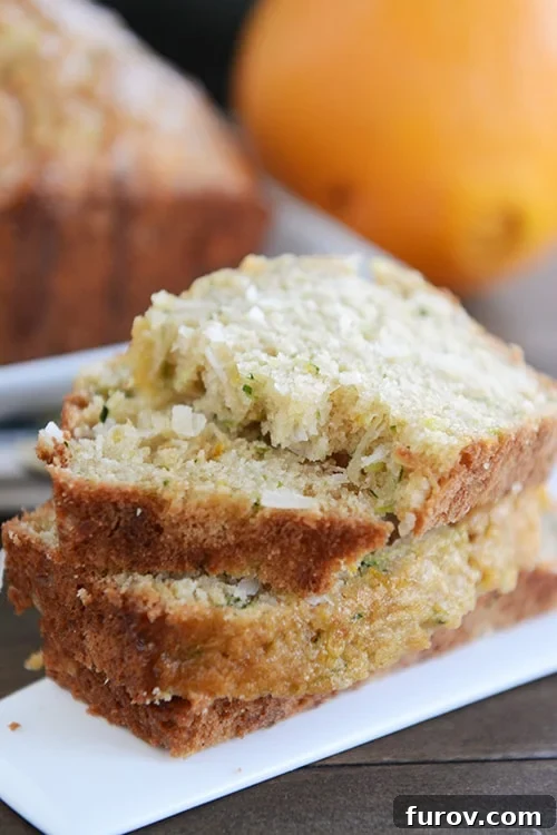 Thick slices of orange zucchini bread stacked on top of each other, showcasing the moist crumb and vibrant glaze.