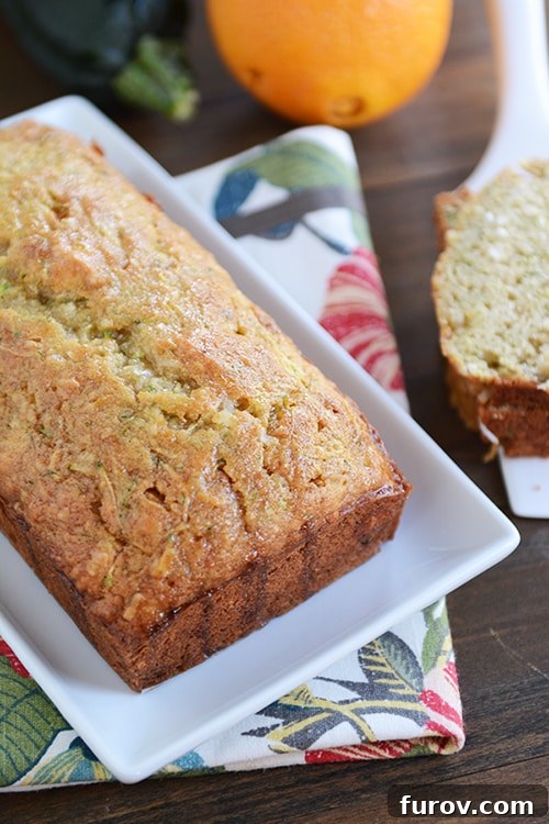 A perfectly baked loaf of glazed orange zucchini bread resting on a white platter, ready to be sliced.