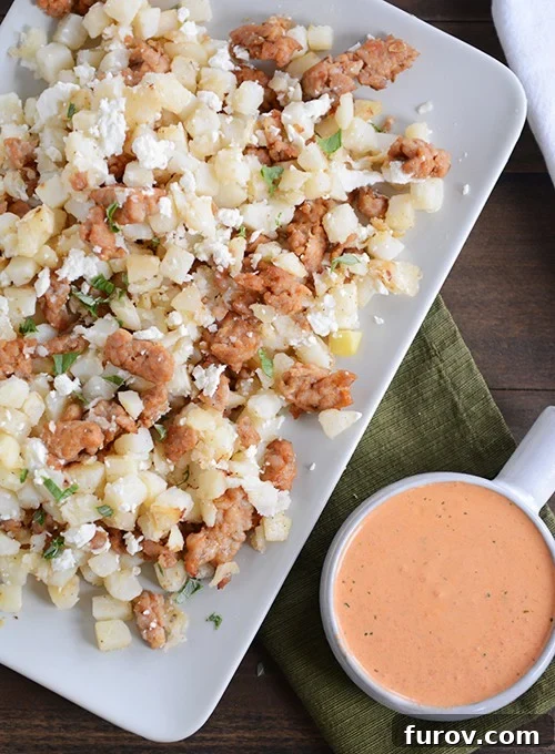 Vibrant Pesto Roasted Pepper Hash Browns 2 Top down view of a white tray of cubed potatoes and sausage next to a bowl of red pepper sauce.