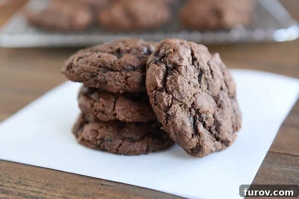 Four freshly baked Triple Chocolate Zucchini Cookies cooling on a sheet of parchment paper, showcasing their rich, dark color and soft appearance.