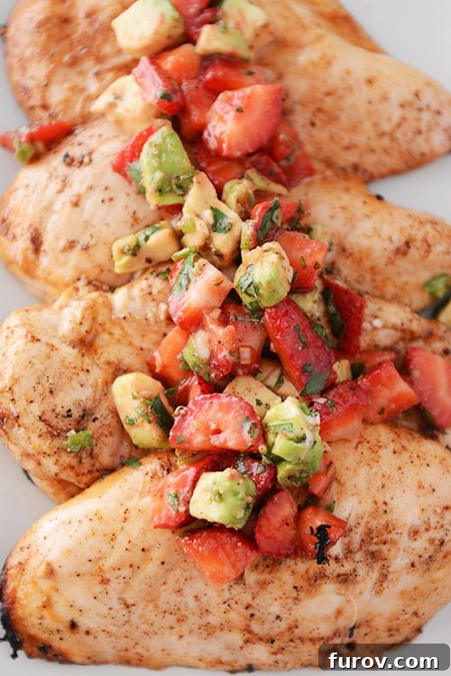 Four large grilled chicken breasts, each generously topped with a spoonful of bright strawberry-avocado salsa, ready to be served.
