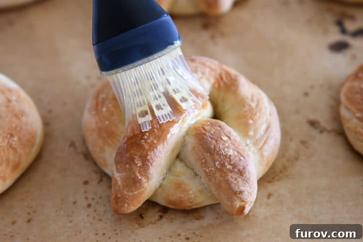 Pillowy Soft Homemade Pretzels 11 A pastry brush applying generous amounts of melted butter onto a hot, freshly baked soft pretzel.