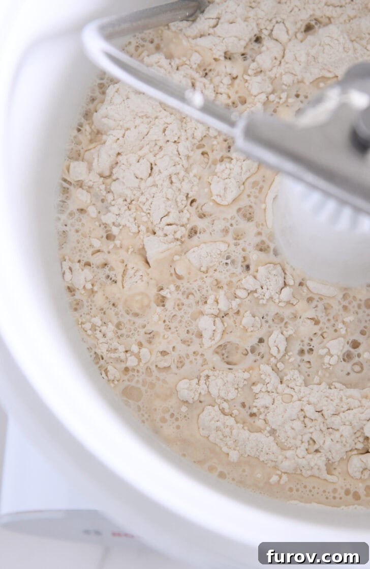 Pillowy Soft Homemade Pretzels 3 Mixing bowl of a white Bosch universal mixer with flour, water, and yeast ingredients, ready for dough preparation.